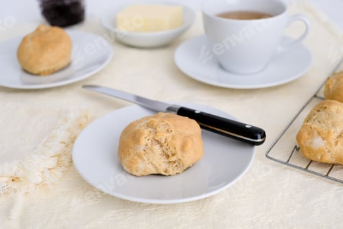Preview: Homemade buns on plates with a butter knife and a cup of tea
