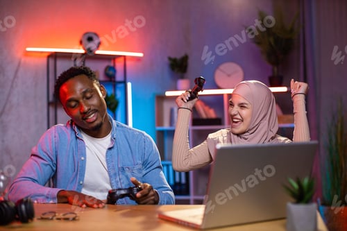 Preview: Happy multi ethnic couple using laptop for playing games