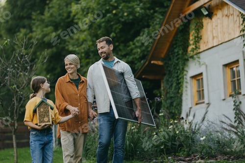 Preview: Family walking in garden holding solar panel. Solar energy and sustainable lifestyle of young family