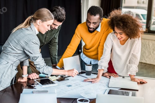 Preview: multicultural businesspeople looking at blueprint in office