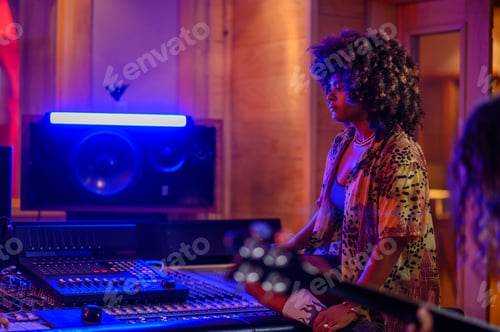 Preview: A musician standing next to a mixing console in a studio with a guitar player
