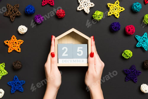 Preview: Top view of female hands holding calendar on black background. The twenty fifth of December.
