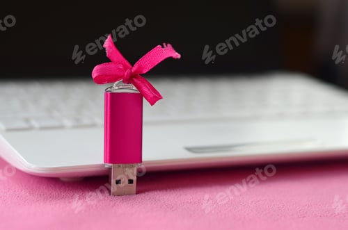Preview: Brilliant pink usb flash memory card with a pink bow lies on a blanket