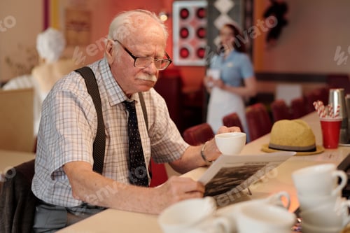 Preview: Elderly Man Reading Newspaper While Holding Cup of Coffee