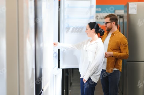 Preview: Young couple, satisfied customers choosing fridge in appliances store