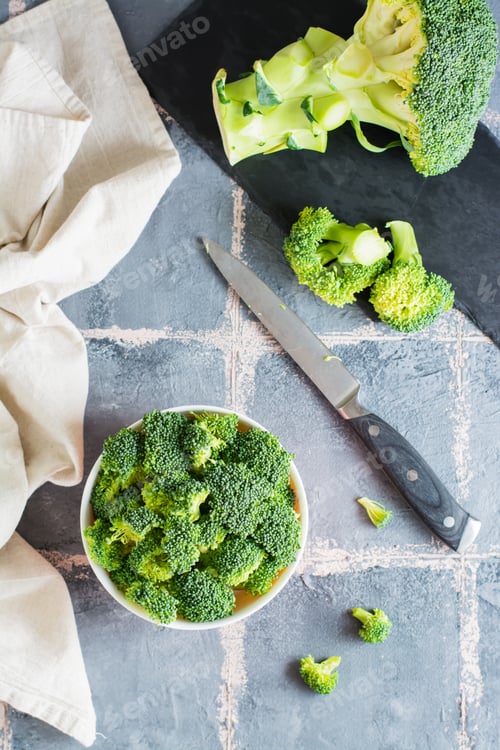 Preview: Pieces of raw broccoli in a bowl and a knife on the table. Vertical view.