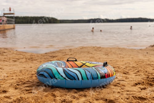 Preview: A vibrant inflatable tube lies on soft sand by the water's edge.