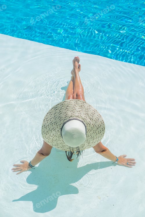 Preview: Woman sitting in a swimming pool in a sunhat