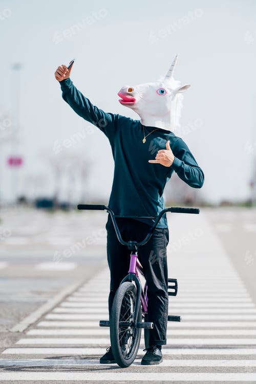 Preview: Man wearing unicorn mask taking a photo with smartphone