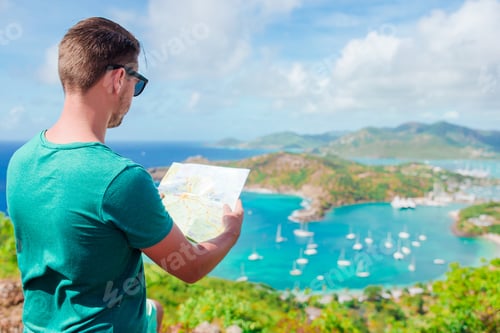 Preview: Young tourist man with map background of English Harbor from Shirley Heights, Antigua, paradise bay