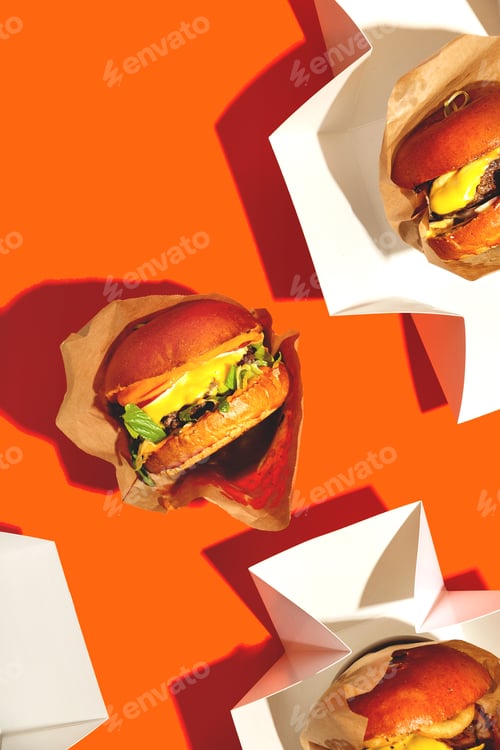 Preview: Big burger with cheese in a package on a bright orange background. Fast food delivery. Top view.
