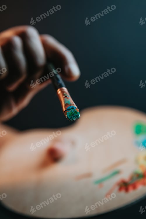Preview: Hands of old female artist holding messy dirty paint brushes with different paints in art studio