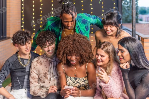 Preview: A group of multi-ethnic friends looking to a phone on a terrace while drinking