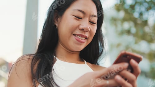 Preview: Cute brunette girl sits on bench on the street with smartphone in her hands, looks around