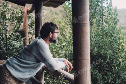 Preview: One thoughtful man relaxing outside home in terrace wooden patio and looking green nature background