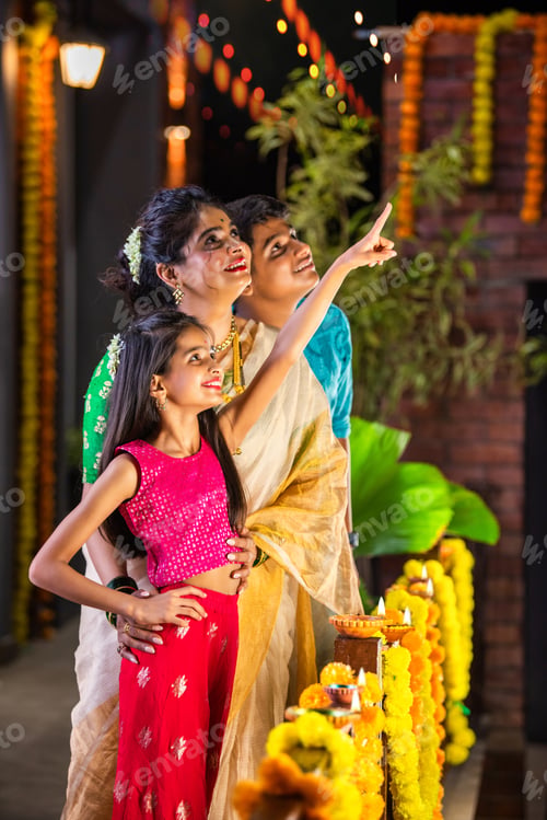 Preview: Indian family celebrating Diwali, with a young girl pointing at fireworks in the night sky