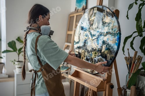 Preview: Female artist proudly looking at canvas on easel with finished handwork made of epoxy resin.