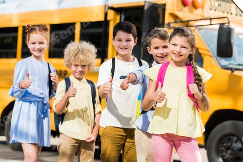 Preview: group of happy pupils looking at camera and showing thumbs up in front of school bus