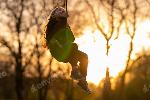 Preview: Happy childhood. Smiling little girl swings on homemade swing in nature, in village in sunset