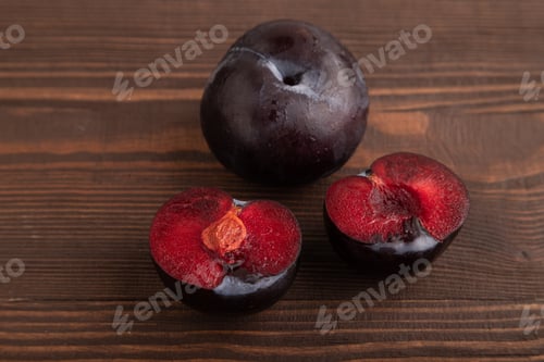 Preview: Purple Plum Cut in half on brown wooden, Side view, close up
