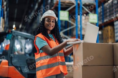 Preview: Female warehouse worker using laptop smiling at camera