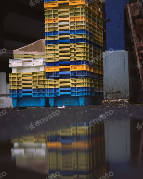 Preview: Stack of colorful plastic crates reflected in a puddle in a fisher habor