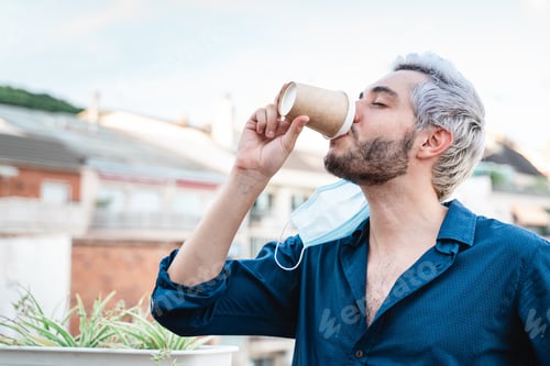 Preview: Happy young business man drinking coffee with opened safety mask - Focus on right hand