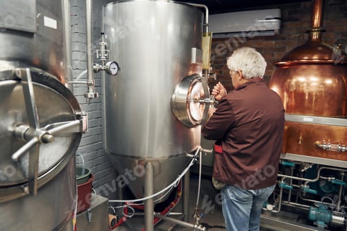 Preview: Retro style. Senior man is standing in the storage with equipment for beer