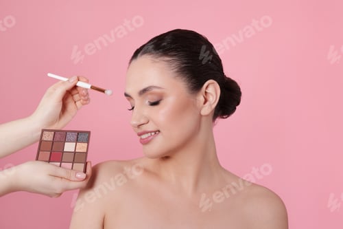 Preview: Makeup artist applying eyeshadows onto woman's face on pink background, closeup