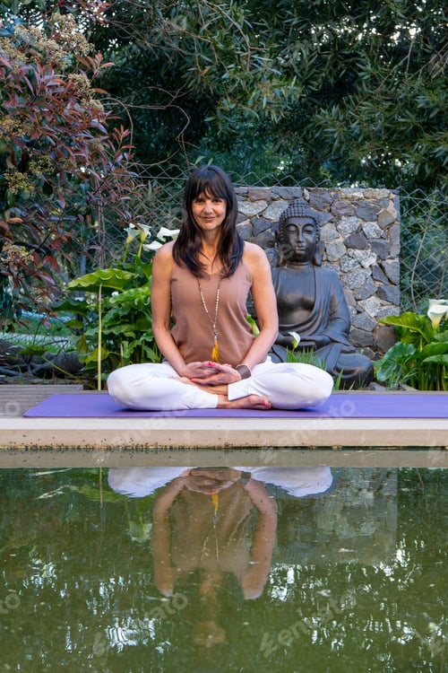 Preview: Mid-adult woman smiling while meditating in front of a Buddha statue