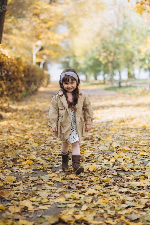 Preview: Happy and beautiful little girl in a beige coat walks in the autumn park