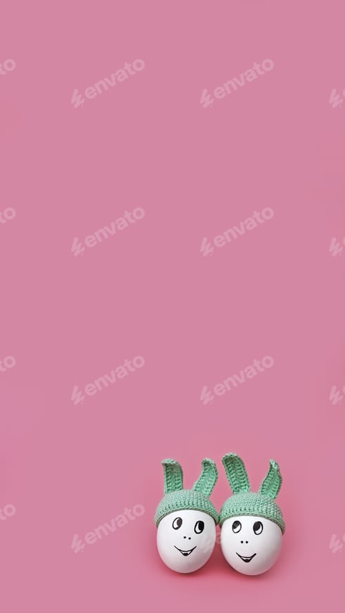 Preview: two white eggs in beanie with rabbit ears and cheerful faces on pink background