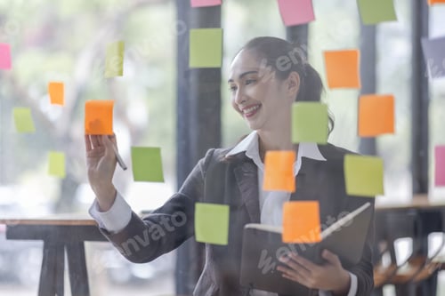 Preview: Young Serious Asian Creative team use post it notes to share idea sticky note on glass wall. Asian b