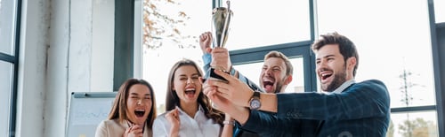 Preview: panoramic shot of excited multicultural businesswomen and businessmen looking at trophy in office
