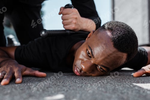 Preview: selective focus of detained african american man lying on ground near police officer with baton,