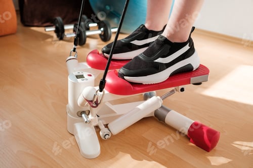 Preview: Close female legs doing cardio on the stepper with ball, and dumbbells on the background. Workout at