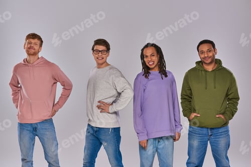 Preview: young multiracial friends in casual attire standing with hands akimbo on grey backdrop, diversity
