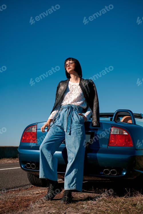 Preview: Young stylish woman with a haircut standing near roofless car outdoors