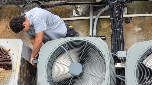Preview: Young man Millennial is HVAC technician working on outdoor air conditioners exposed to weather.