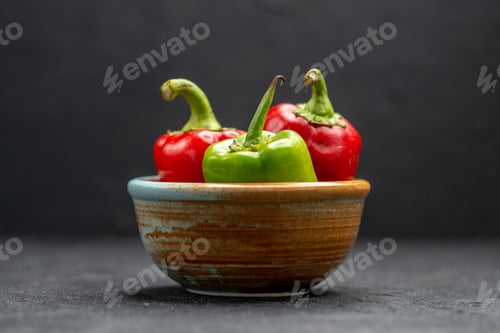 Preview: side close view of brown bowl of bell peppers in the center on dark grey table and blurred dark