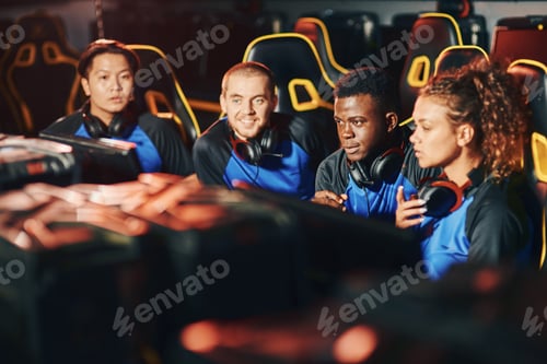 Preview: Professional multiracial cybersport team sitting together in gaming club or internet cafe, looking