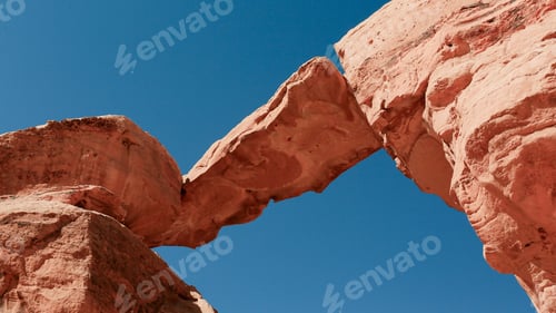 Preview: Natural rock formation arching over sandy landscape in Wadi Rum Desert, Jordan during clear blue sky