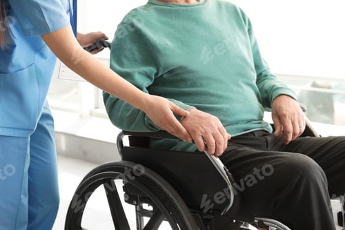 Preview: Nurse assisting senior man in wheelchair at hospital, closeup