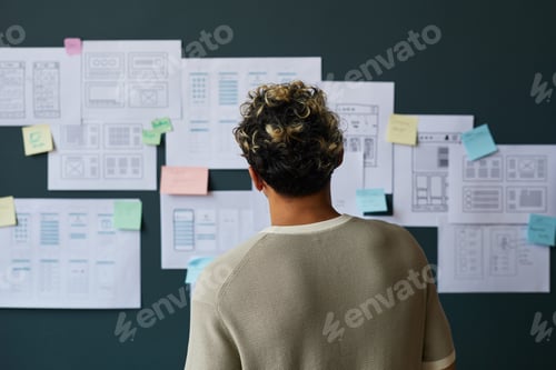 Preview: Young Adult Caucasian Man Analyzing Wireframe Sketches on Wall in Office