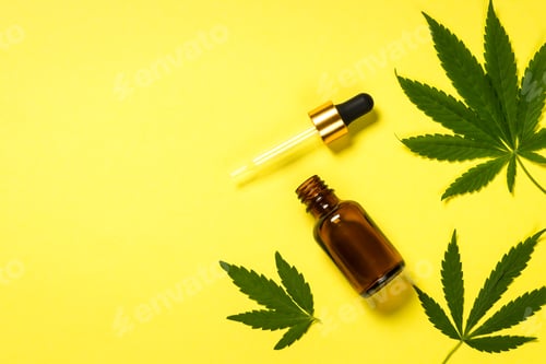 Preview: Cannabis oil and green leaves at yellow table