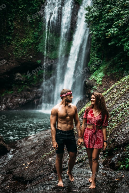 Preview: An athletic man holds the hand of a beautiful woman at a waterfall. A couple in love on a waterfall