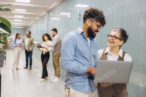 Preview: Business people collaborating on laptop in office hallway