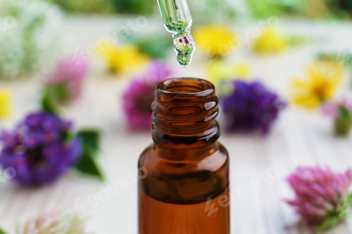Preview: Dripping essential oil from pipette into bottle on white wooden table, closeup