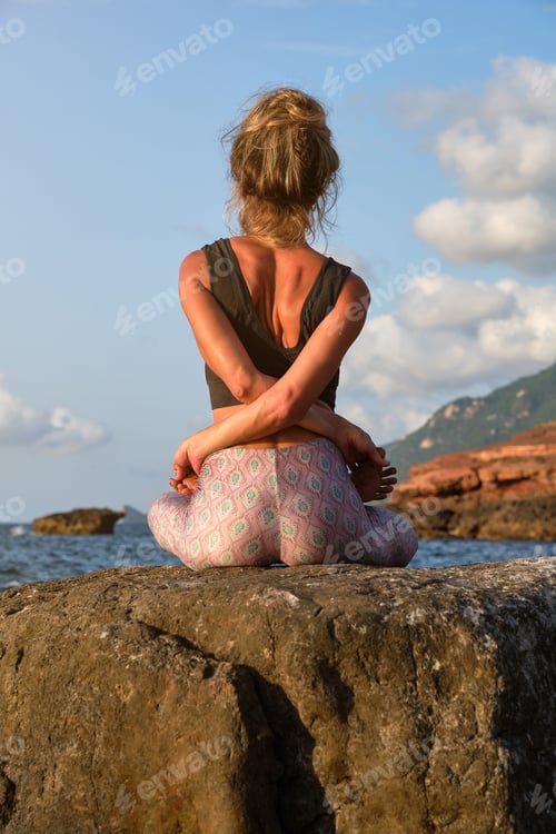 Preview: Woman meditating in Bound Lotus pose on rock
