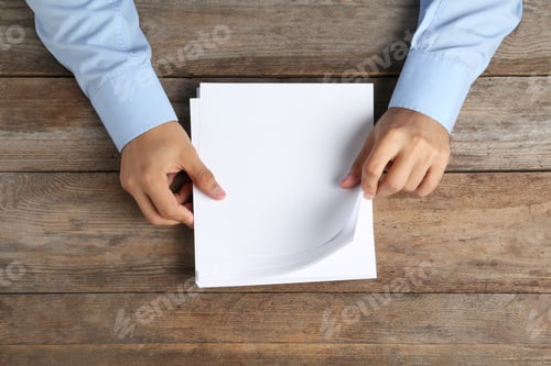 Preview: Man holding blank paper sheets for brochure at wooden table, top view. Mock up